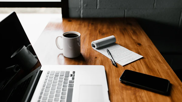 Desk with a laptop, notebook, coffee mug and phone