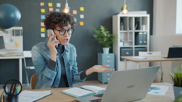 Woman on a phone call at a desk with a laptop