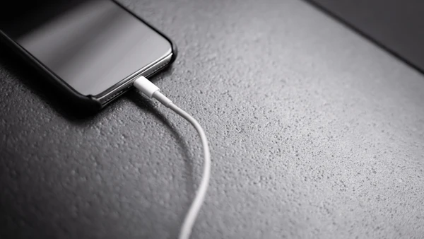 Smartphone connected to a charging cable on a grey surface