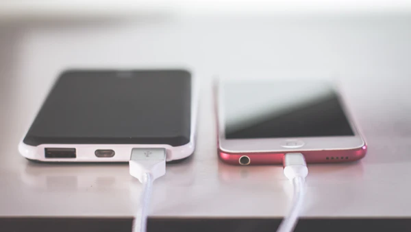 Two smartphones charging side by side on a white table